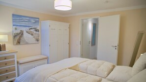 A bedroom with a bed, a dresser, a wardrobe, and a painting of a beach scene. - Südstrand Apartment - your modern hideaway for a relaxing Baltic Sea vacation (Grömitz)