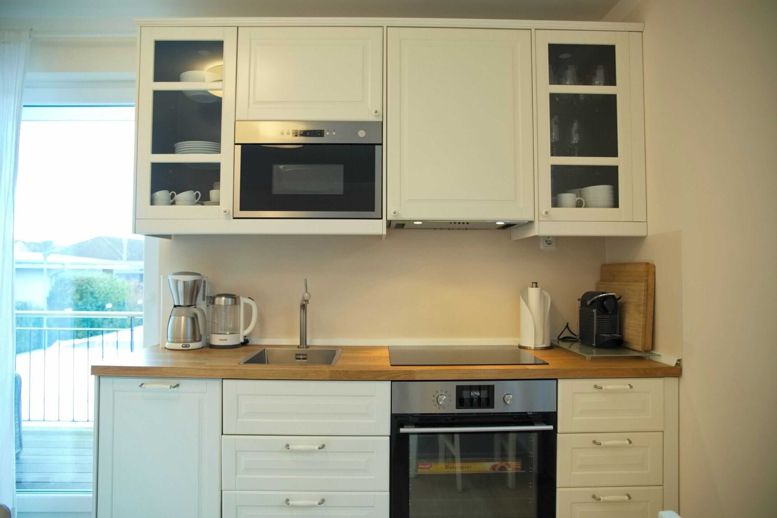 A compact kitchen with white cabinets, a built-in oven, a coffee maker, and a toaster.
