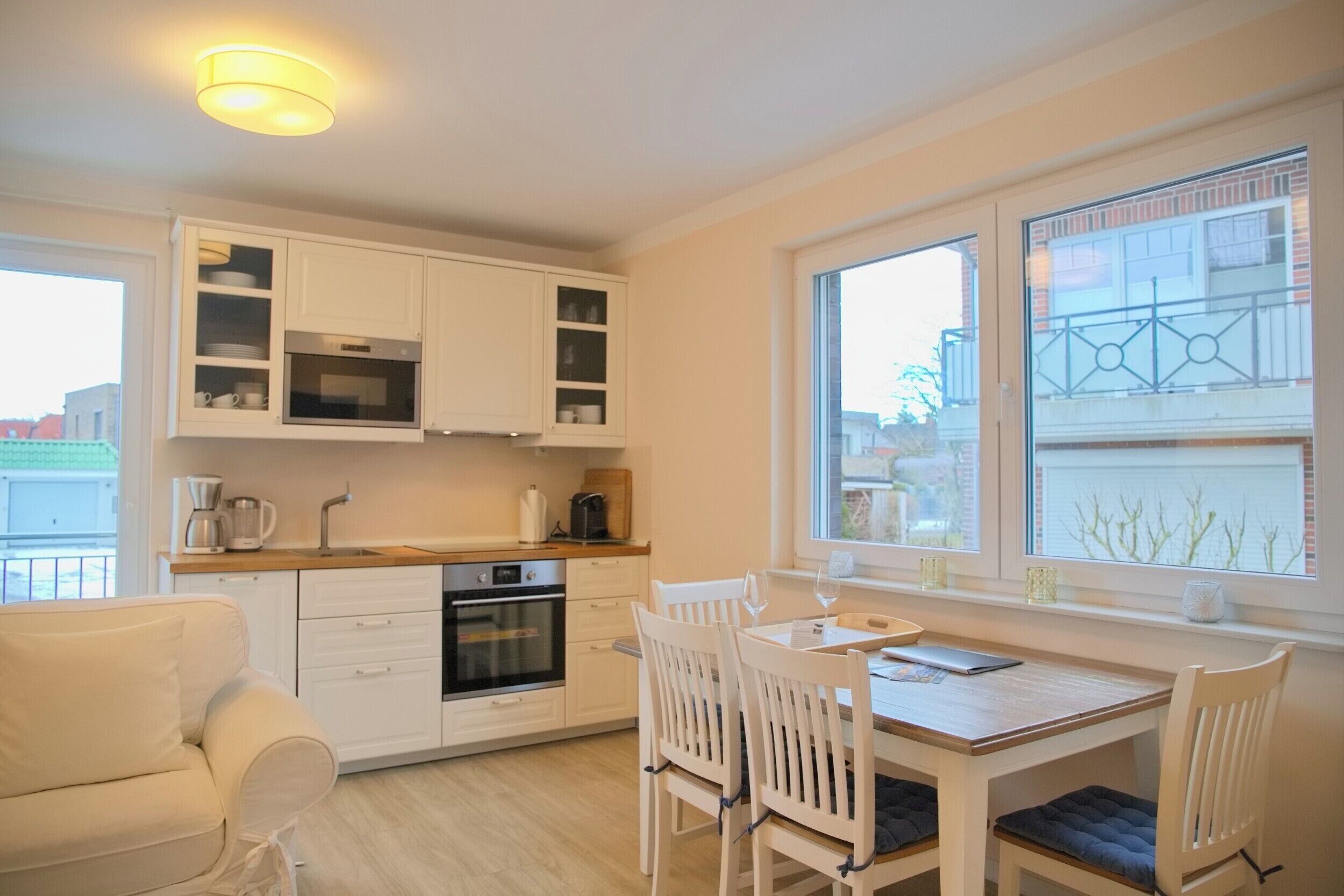 Een moderne keuken met witte kasten, een eettafel met stoelen en een groot raam met uitzicht op gebouwen.