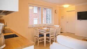 A compact kitchen with a dining area, a white sofa, and a TV mounted on the wall. - Südstrand Apartment - your modern hideaway for a relaxing Baltic Sea vacation (Grömitz)