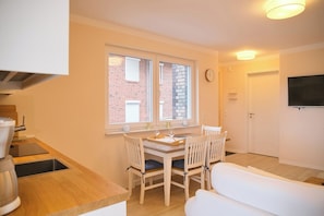 A compact kitchen with a dining area, a white sofa, and a TV mounted on the wall. - Südstrand Apartment - your modern hideaway for a relaxing Baltic Sea vacation (Grömitz)