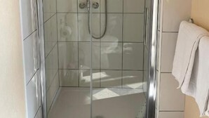 Ένα ντους με γυάλινο περίβλημα, με μια κεφαλή ντους που κρατιέται στο χέρι και μια βρύση τοποθετημένη στον τοίχο.