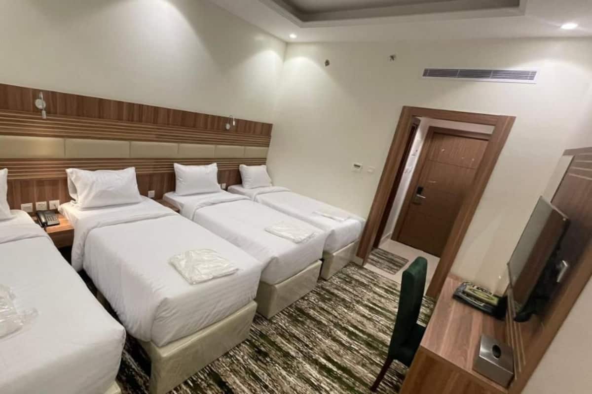 A hotel room with three single beds, a wooden headboard, a TV, and a small desk with a chair.