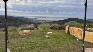 Un'area erbosa con rocce e un piccolo oggetto bianco, con vista su una località costiera e il mare.