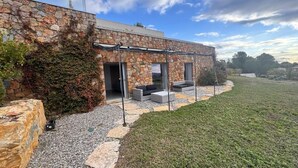 Un edificio moderno in pietra con un'area salotto all'aperto coperta e un prato.