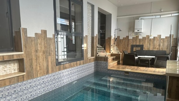 A modern indoor pool area with a clear pool, wooden accents, and a seating area with a sofa and chairs. - Belgaïd - T4 high standing, heated indoor pool for families only (Bir El Djir)