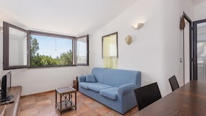Una sala de estar moderna con un sofá azul, una mesa de madera y un amplio ventanal con vistas a zonas verdes.