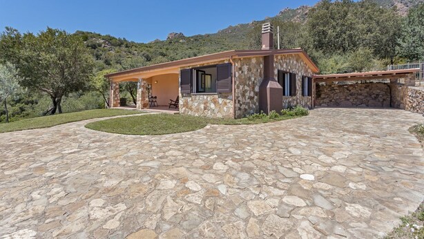 Una casa de piedra con un patio, rodeada de árboles y colinas.