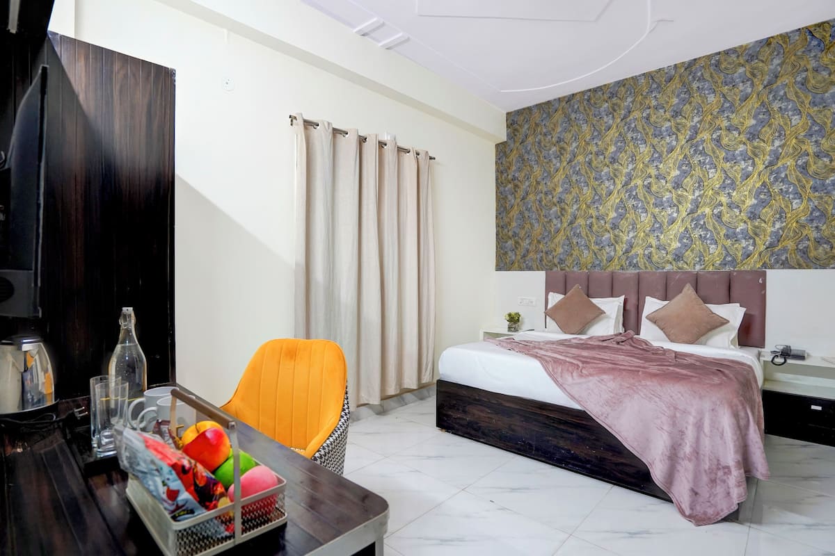 A hotel room with a bed, a desk with a chair, a television, and a window with curtains.