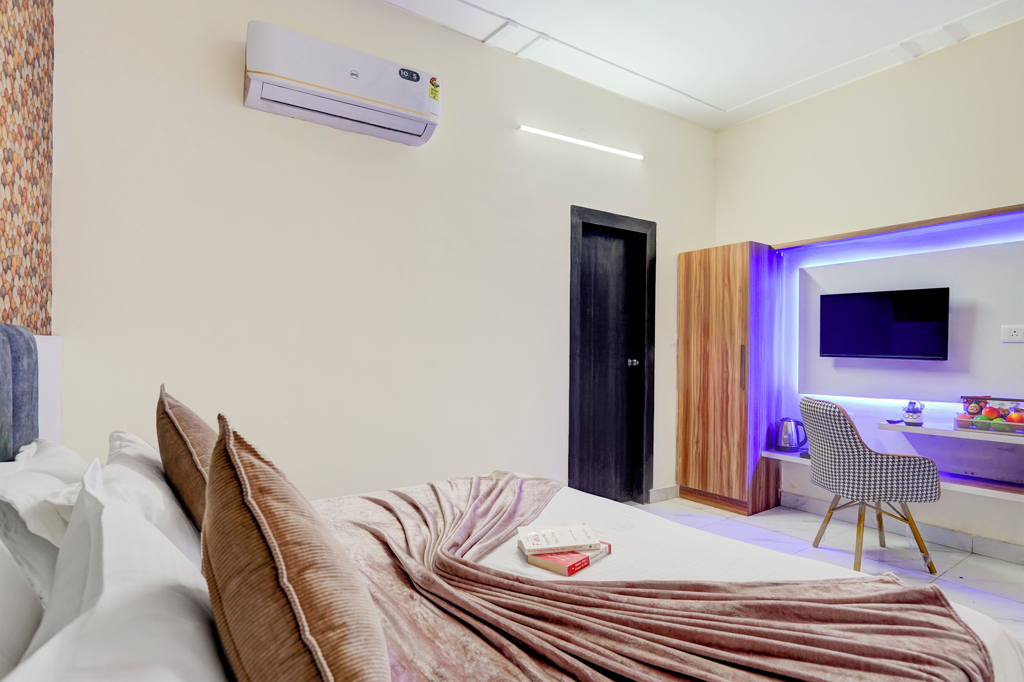 A modern hotel room with a bed, a desk with a chair, an air conditioning unit, and a television.
