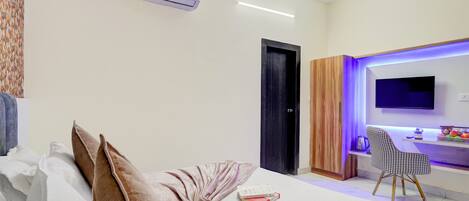 A modern hotel room with a bed, a desk with a chair, an air conditioning unit, and a television.