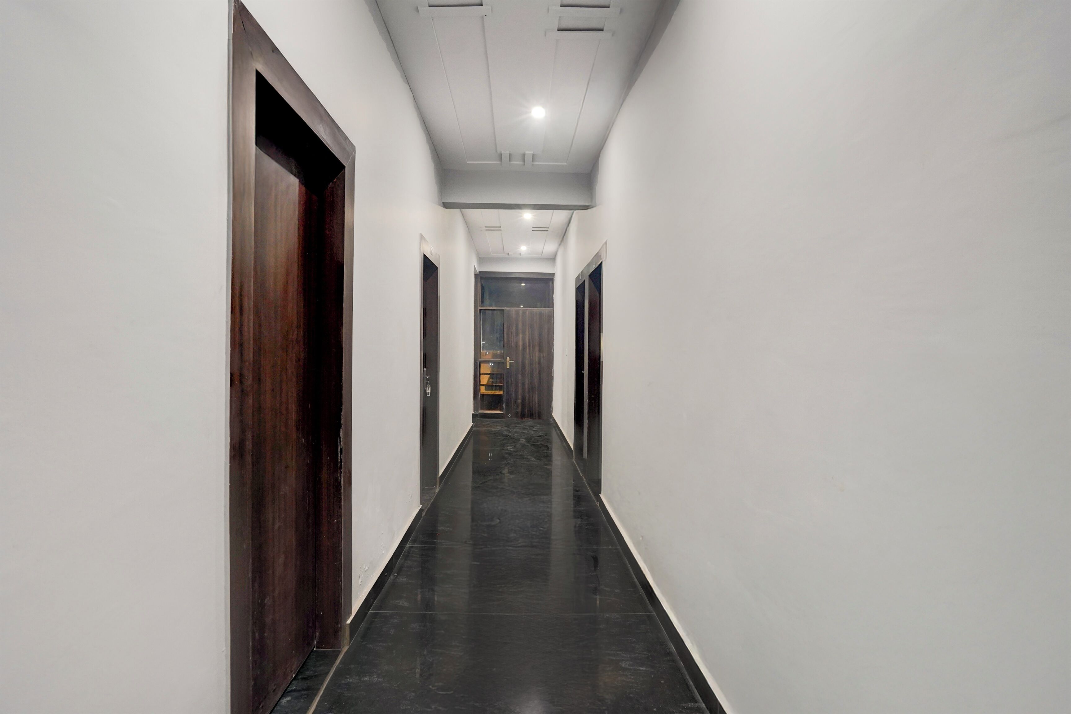 A long, narrow hallway with dark wooden doors on one side and white walls on the other.