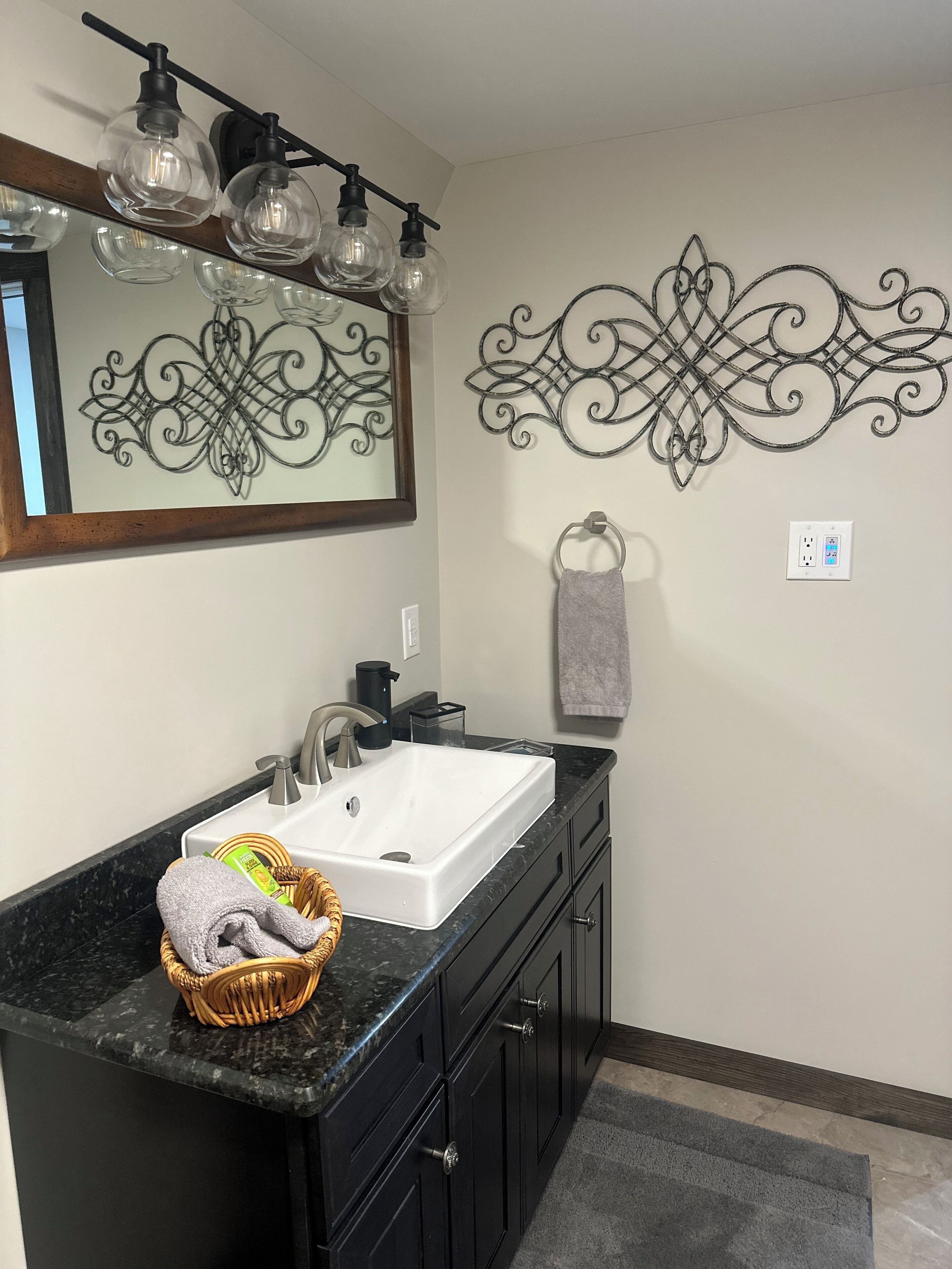A bathroom with a white sink, black cabinets, a wicker basket, and decorative wall art.