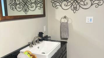 A bathroom with a white sink, black cabinets, a wicker basket, and decorative wall art.