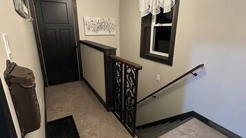A hallway with a door labeled "PRAYER CLOSET," a window with white curtains, a wall-mounted artwork, and a staircase with a black railing.