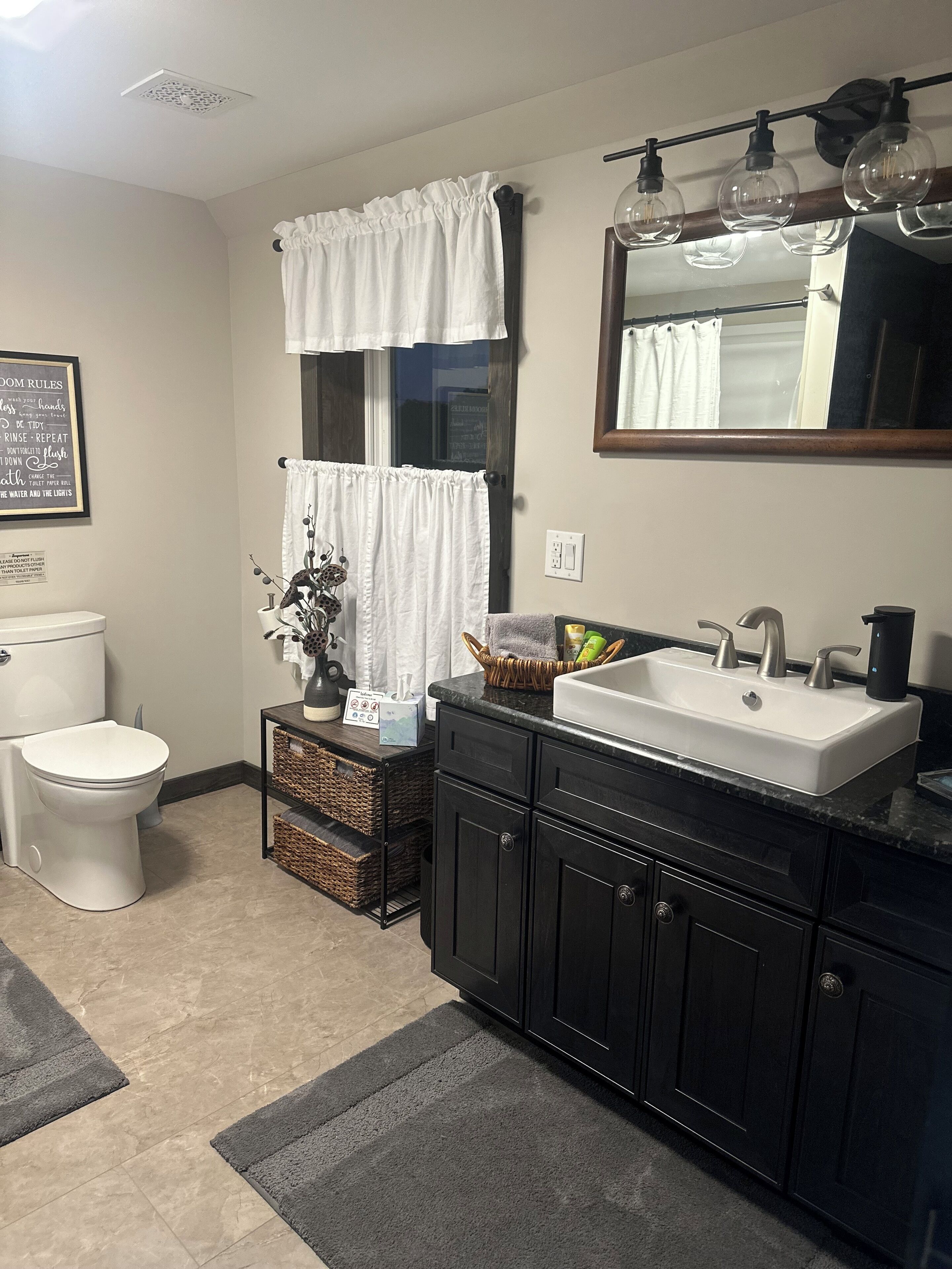A bathroom with a toilet, sink, and mirror. There is a basket with toiletries and a sign on the wall.