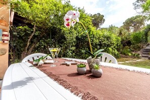 A table set outdoors with a white chair, a tablecloth, and a potted plant. - La Marina Guest House – Garden – Wi-Fi – Very close to the sea (Arboriamar)