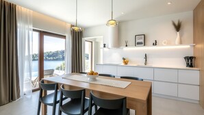 A modern kitchen with white cabinets, a wooden dining table, and a view of the sea. - Villa Cristal Blue by Villas Guide (Blato)