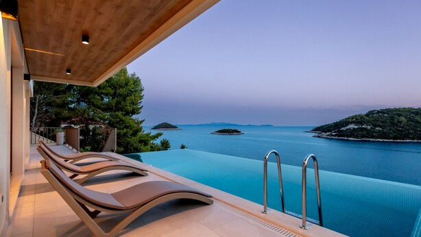 An infinity pool with a view of the sea and islands, accompanied by lounge chairs and a wooden ceiling. - Villa Cristal Blue by Villas Guide (Blato)