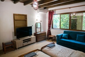A bedroom with a bed, a TV, a dresser, a mirror, a window with curtains, and a blue sofa. - Koksinou Apartment 2 (96W9+4H Koskinou, Greece)