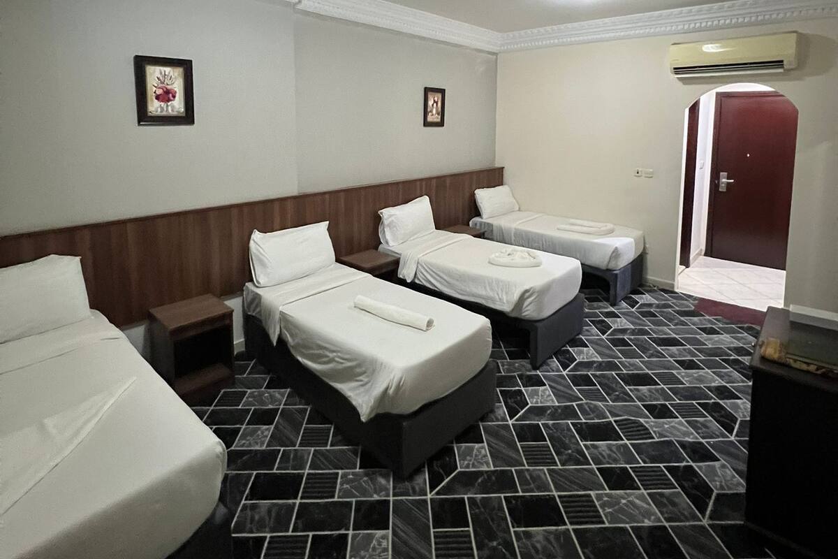 Una habitación de hotel con cuatro camas, suelo de baldosas de mármol y una puerta roja.