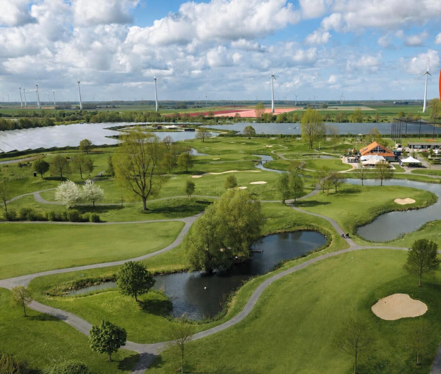 Un parcours de golf avec des étangs, des arbres et des éoliennes en arrière-plan.