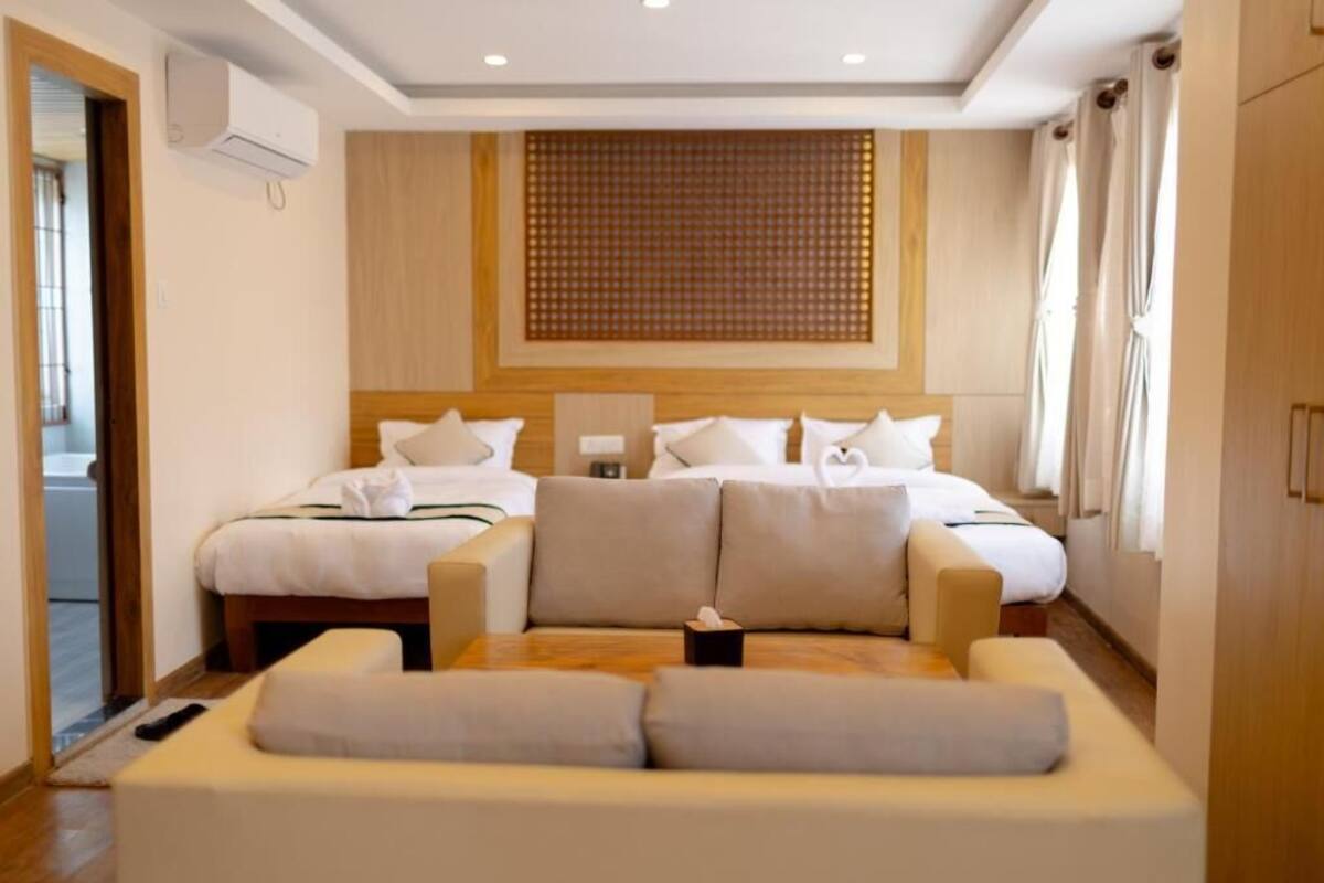 A hotel room with two beds, a sofa, a wooden headboard, and a window with curtains.
