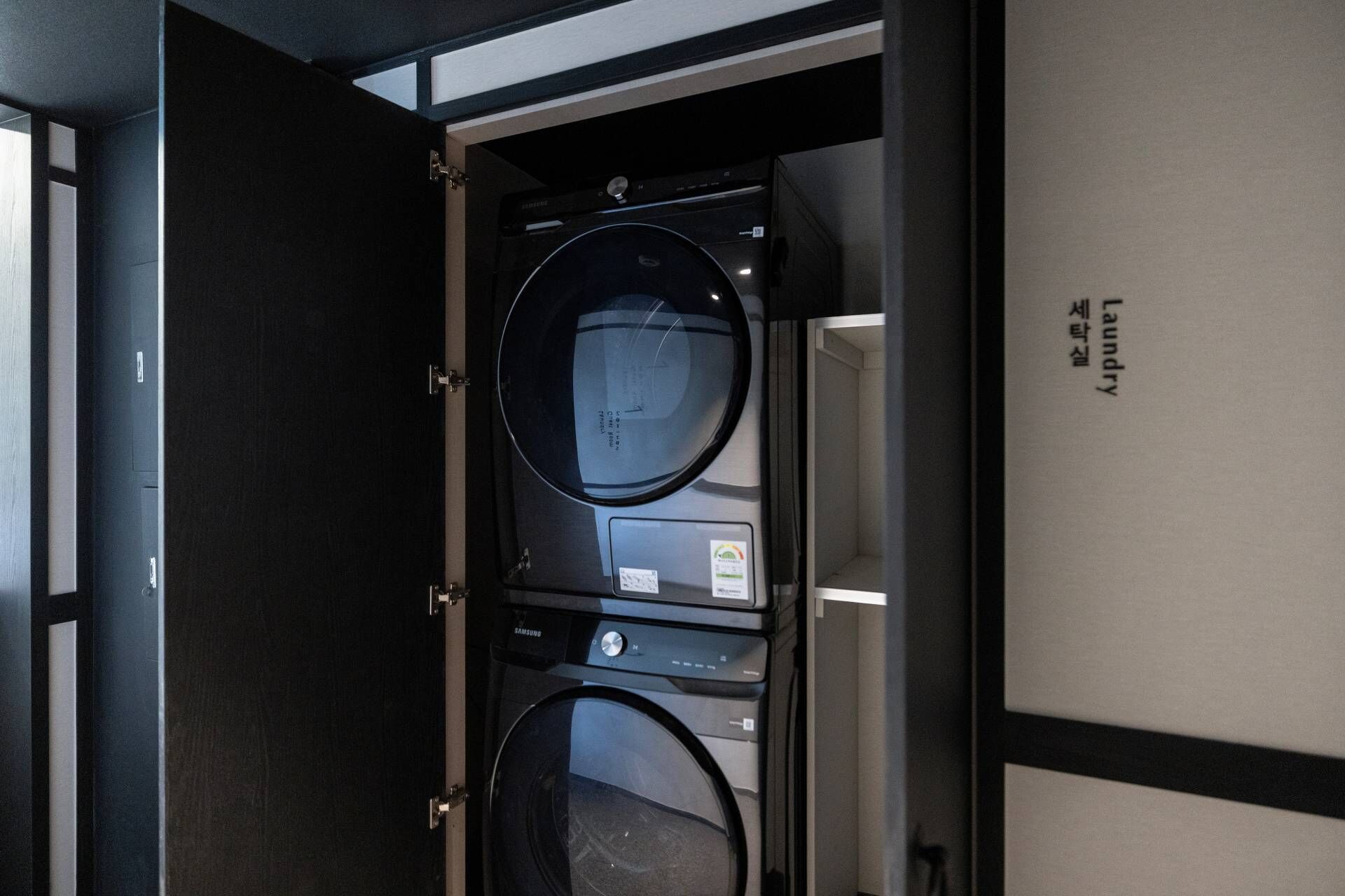 A laundry room with a Samsung washing machine and dryer, a control panel, and a door with a label.