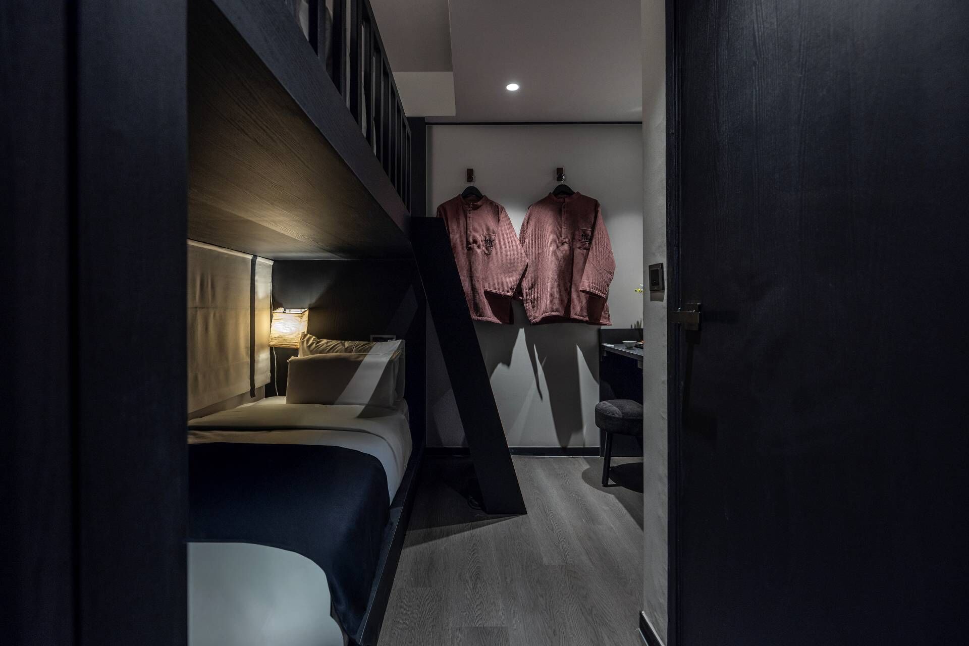A compact bedroom with a bunk bed, a bedside lamp, and a small seating area.