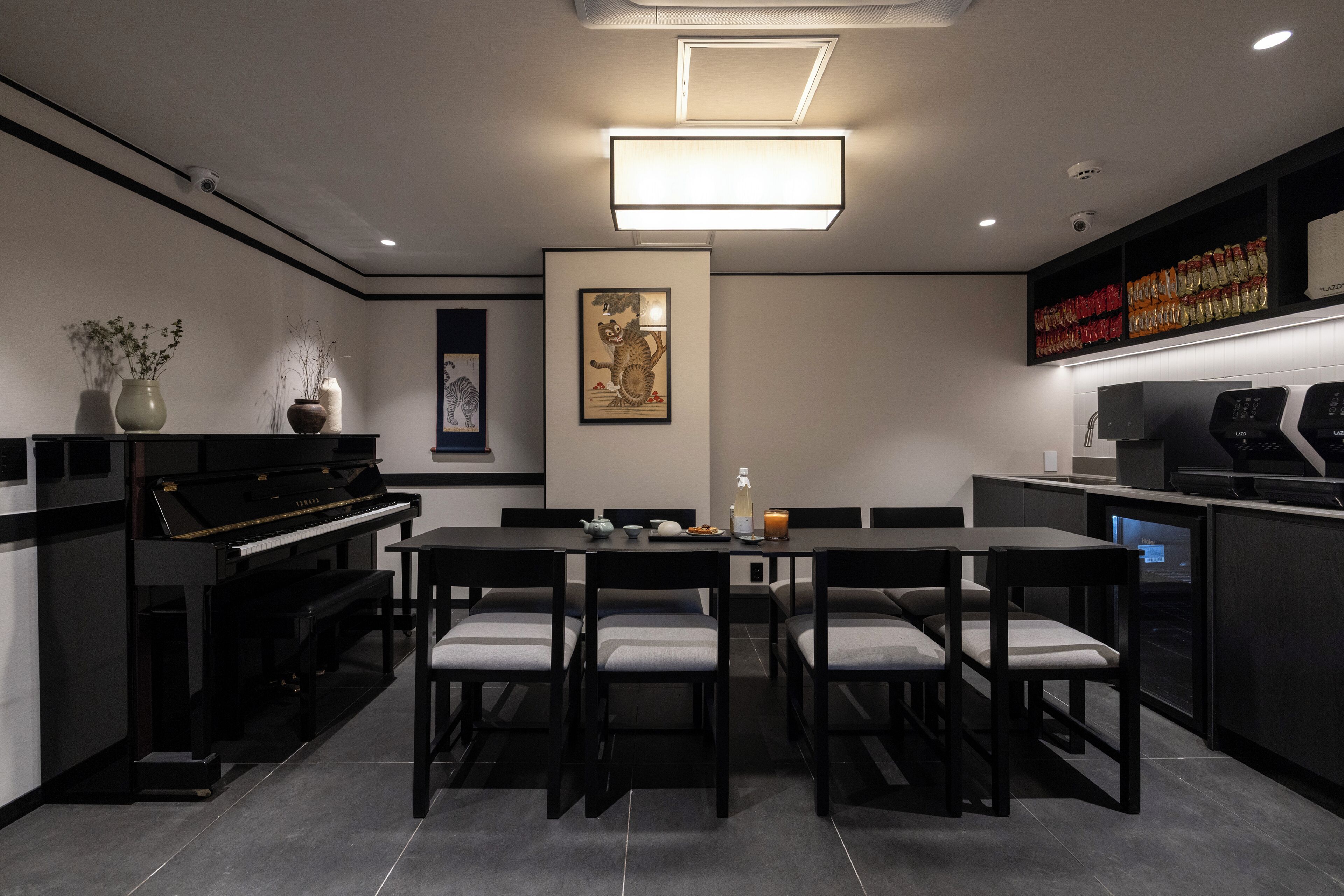 A modern kitchen with a dining area, featuring a piano, a large table with chairs, and a wall-mounted shelf with food items.