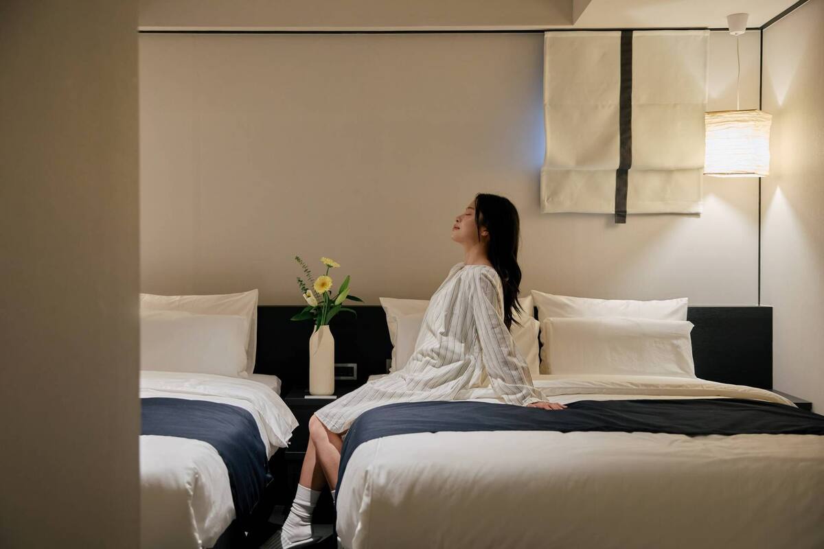 Ein Hotelzimmer mit zwei Betten, einem Nachttisch mit Blumenvase und einer Wandleuchte.