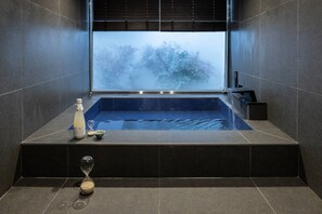 Un bagno moderno con una vasca da bagno grande, una finestra con persiane e una piccola clessidra sul pavimento.