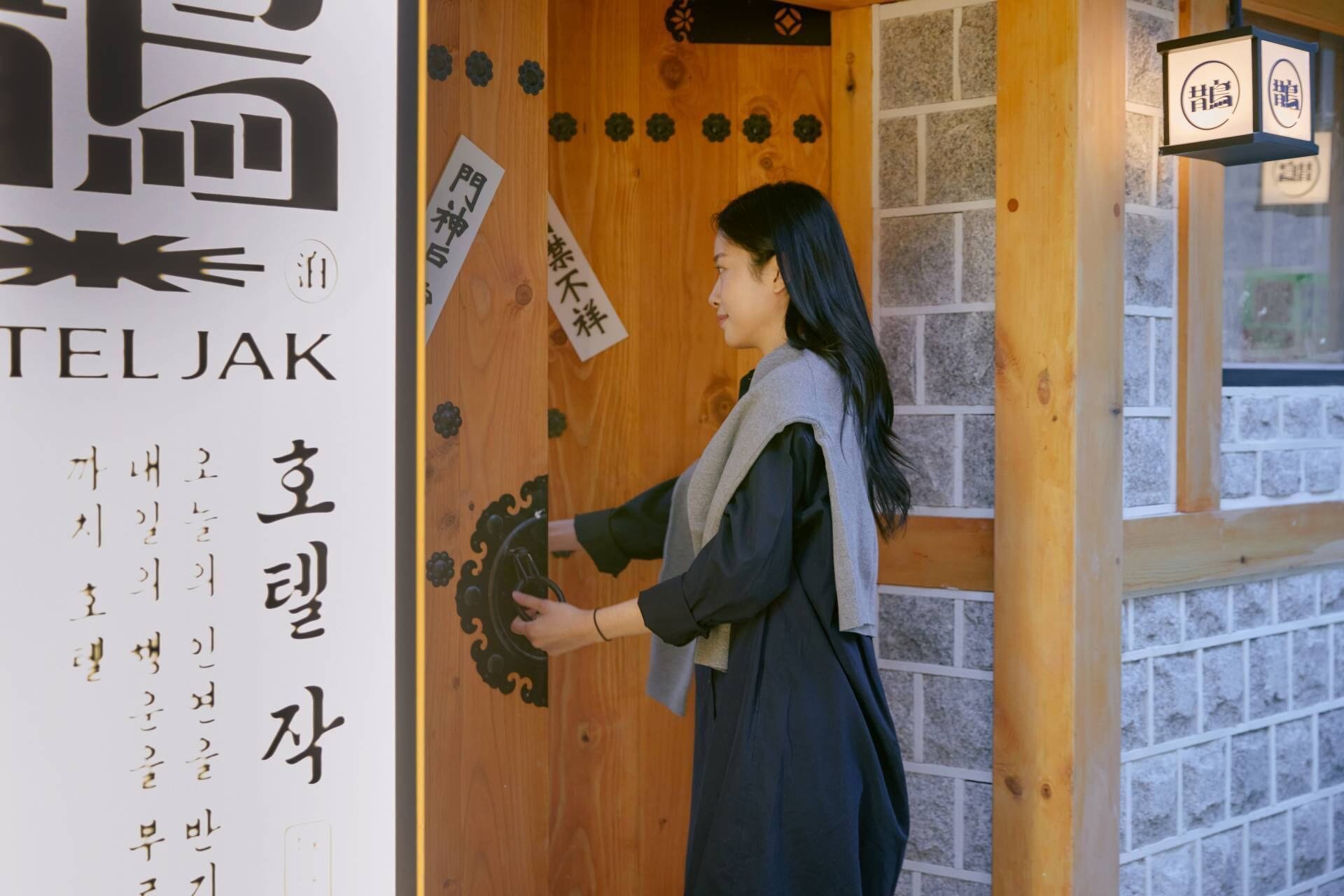 A person opening a wooden door with a sign that reads "TELJAK" and another sign with Japanese characters.