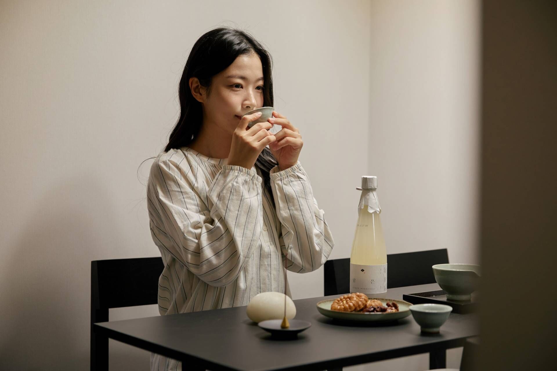 A person sitting at a table with a bottle, a bowl, and a plate of food.