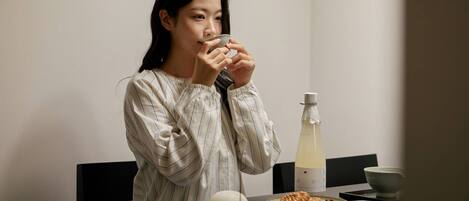 A person sitting at a table with a bottle, a bowl, and a plate of food.