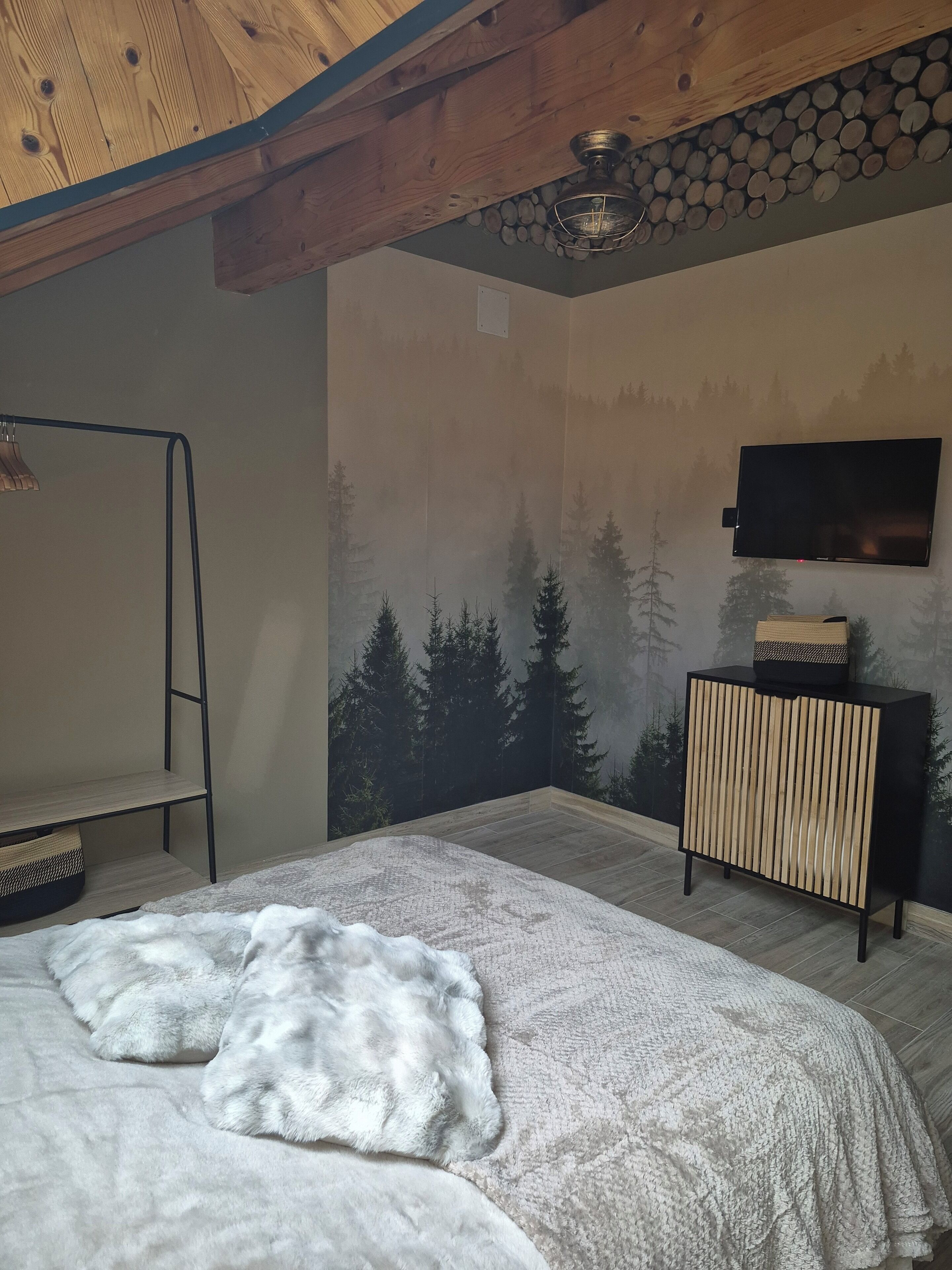 Un dormitorio con cama, techo de madera, televisor montado en la pared y mesita de noche.
