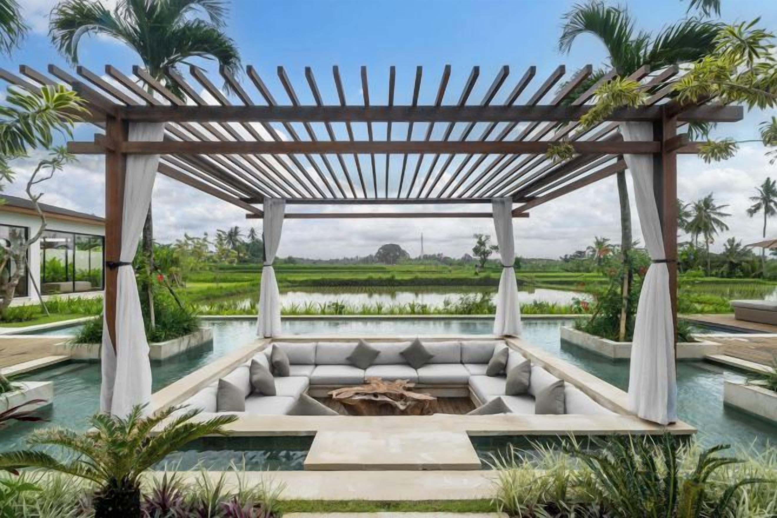 A covered outdoor seating area with a pool, surrounded by greenery and palm trees.