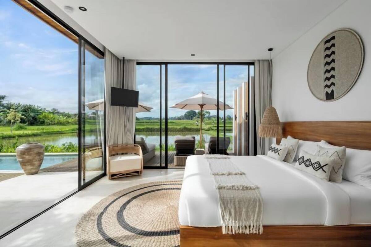 A bedroom with a large bed, a TV, and a view of a lake and greenery.