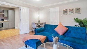 A modern living room with a blue sofa, a coffee table, and a dining area in the background. - 2BR Ground Floor • Parking • Central By Tempstay (Windsor)
