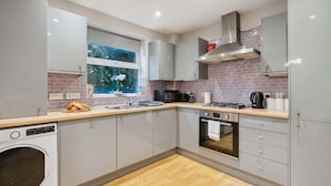 A modern kitchen with grey cabinets, a stainless steel range hood, a built-in oven, and a window with a view of greenery. - 2BR Ground Floor • Parking • Central By Tempstay (Windsor)