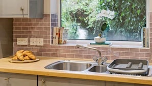A kitchen with a window, a sink, and a countertop with a tray and a bowl of croissants. - 2BR Ground Floor • Parking • Central By Tempstay (Windsor)
