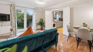 A modern living room with a teal sofa, a dining area with a table and chairs, and a kitchen in the background. - 2BR Ground Floor • Parking • Central By Tempstay (Windsor)
