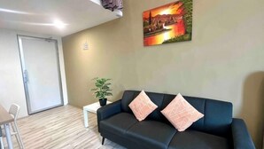 A room with a dark blue sofa, a small white table, a potted plant, and a painting on the wall. - The CEO Suite7 by Homey Planet (Bayan Lepas)
