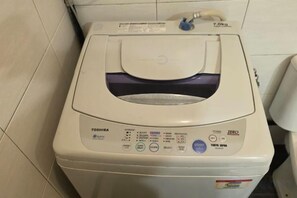 Una lavadora Toshiba blanca con panel de control, una entrada de agua y una manguera de desagüe.