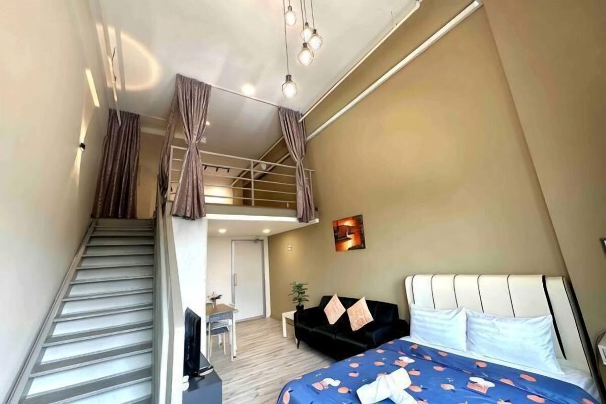 A bedroom with a bed, a desk, a chair, a staircase, and a balcony.