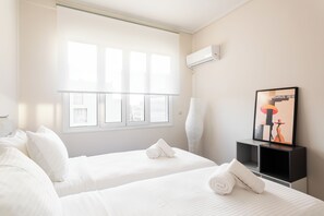 Een hotelkamer met twee bedden, een raam, een airconditioning en een prent in een lijst, plus een nachtkastje.