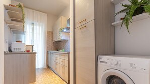 Une cuisine compacte équipée d’un lave-linge, de meubles en bois et d’un plan de travail avec un four à micro-ondes.