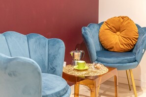 Une pièce avec deux chaises bleues, une petite table sur laquelle se trouvent une tasse verte et un pot en argent, et un coussin de couleur moutarde sur l’une des chaises.