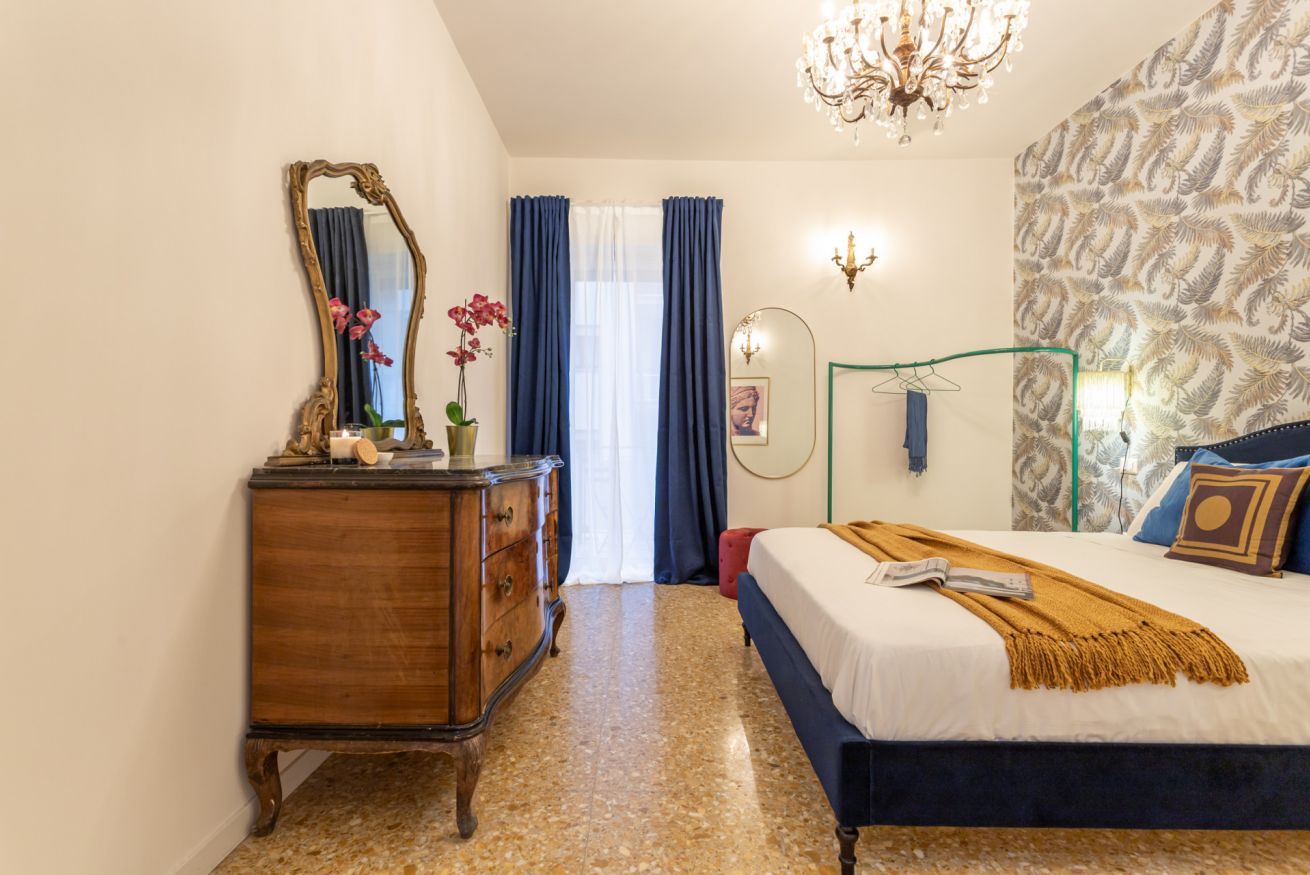 Een slaapkamer met een bed, een kaptafel, een spiegel en een kroonluchter.