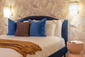 Un lit bien fait, agrémenté d’un couvre-lit à motifs, d’une tête de lit bleue et d’une table de chevet sur laquelle repose un livre.